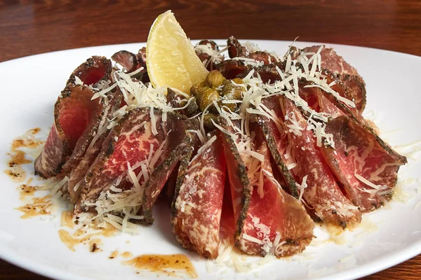carpaccio, füme et ile rendelenmiş peynir, limon, kapari soslu, yatıyor ahşap bir masa üzerinde duran beyaz bir plaka üzerinde yakın çekim