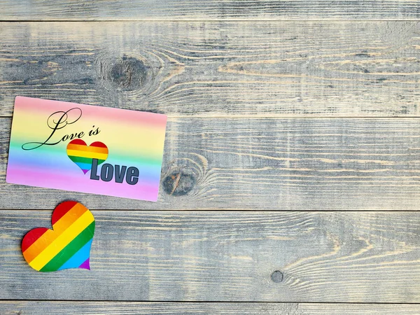 Card on which is written love is love with a rainbow background and a heart with the LGBT flag lie on a light blue textured wooden board, has free space to place design information for congratulations