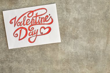 Bir parça kağıt yazıt ile kırmızı ve siyah mürekkeple boyalı Sevgililer günü güzel yazı tipi boyalı. Gri dokulu bir arka plan üzerinde yatıyor. Kart için tasarımcı ekler boş alanı olan.