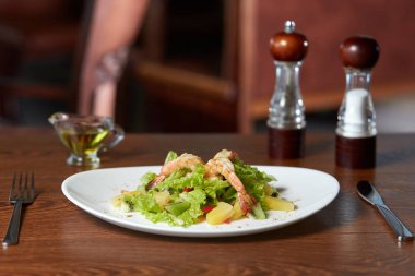 Ananas, dolmalık biber, marul ve çatal bıçak takımı, birlikte bir ahşap yüzeyde tuz, yağ ve biber, menü veya Web sitesi tasarımı için bir arka plan bulanık restoran sandalye üzerinde duran kivi, karides salatası