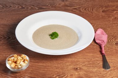 Salantro beyaz bir tabak ve bir tabak kızarmış ekmek kırıntıları ile bir kaşık peçeteye sarılmış yatıyor stand ahşap bir masa ve yanında bir levha ile yulaf çorbası