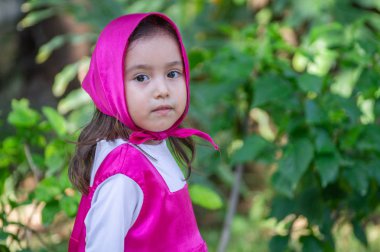Güzel bir kız, beyaz, karizmatik, kahverengi saçlı, siyah gözlü, üç yaşında, pembe giyinmiş, masha tarzı, çok etkileyici, bahçede yürüyor, oyuncak ayı ve çantayla oynuyor. Yeşil çimenler ve ağaçlar