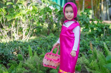 Güzel bir kız, beyaz, karizmatik, kahverengi saçlı, siyah gözlü, üç yaşında, pembe giyinmiş, masha tarzı, çok etkileyici, bahçede yürüyor, oyuncak ayı ve çantayla oynuyor. Yeşil çimenler ve ağaçlar