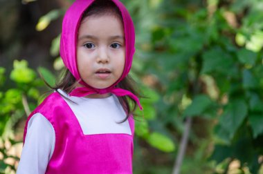 Güzel bir kız, beyaz, karizmatik, kahverengi saçlı, siyah gözlü, üç yaşında, pembe giyinmiş, masha tarzı, çok etkileyici, bahçede yürüyor, oyuncak ayı ve çantayla oynuyor. Yeşil çimenler ve ağaçlar