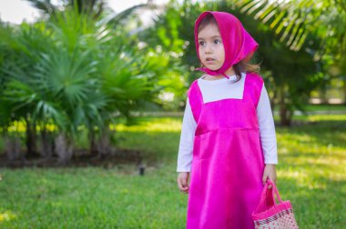 Güzel bir kız, beyaz, karizmatik, kahverengi saçlı, siyah gözlü, üç yaşında, pembe giyinmiş, masha tarzı, çok etkileyici, bahçede yürüyor, oyuncak ayı ve çantayla oynuyor. Yeşil çimenler ve ağaçlar