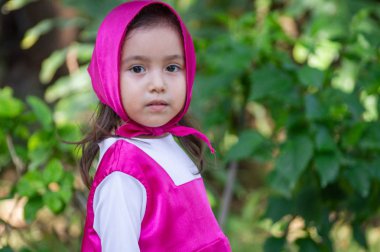 Güzel bir kız, beyaz, karizmatik, kahverengi saçlı, siyah gözlü, üç yaşında, pembe giyinmiş, masha tarzı, çok etkileyici, bahçede yürüyor, oyuncak ayı ve çantayla oynuyor. Yeşil çimenler ve ağaçlar