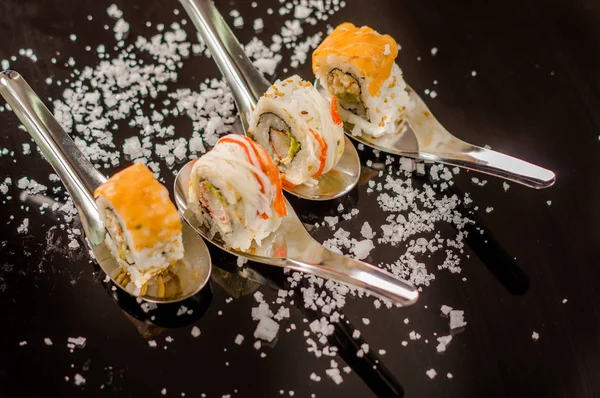 Powyżej widok na pyszne sushi przewraca metalicznych łyżkę z drobnymi ziarenkami soli serwowane na czarny stół — Zdjęcie stockowe