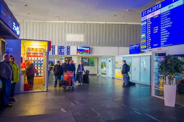 Minsk, Weißrussland - 01. Mai 2018: Unbekannte gehen mit ihrem Gepäck spazieren und beobachten einen Abflugschirm, der sich im Inneren des Flughafens von Minsk befindet — Stockfoto