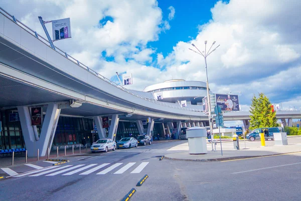 MINSK, BELARUS - 01 DE MAYO DE 2018: Vista al aire libre de los coches estacionados y circulando en la entrada del edificio del aeropuerto de Minsk en un día nublado con una torre de control detrás — Foto de Stock