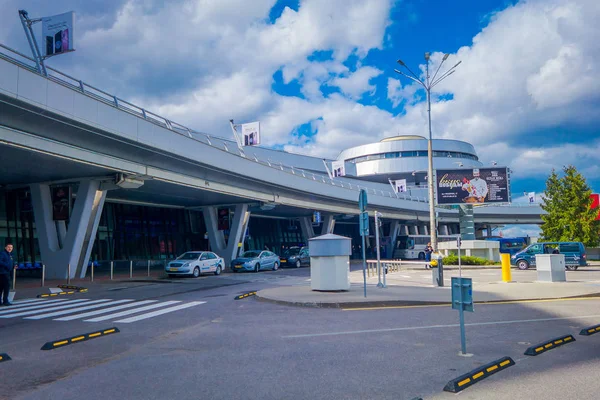 MINSK, BELARUS - 01 DE MAYO DE 2018: Vista al aire libre de los coches estacionados y circulando en la entrada del edificio del aeropuerto de Minsk en un día nublado con una torre de control detrás — Foto de Stock