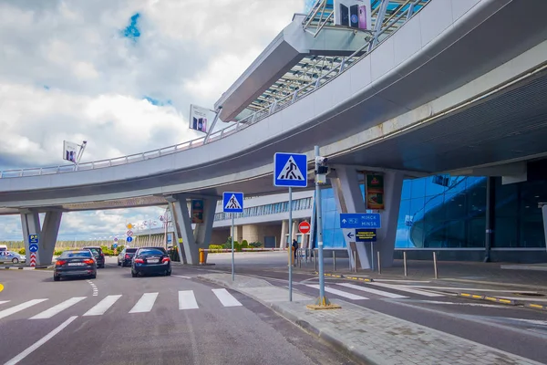 MINSK, BELARUS - 01 DE MAYO DE 2018: Vista de personas caminando y coches estacionados en la entrada del edificio del aeropuerto de Minsk en un día nublado con una estructura de puente apedreado iat la entrada del aeropuerto en Bielorrusia — Foto de Stock