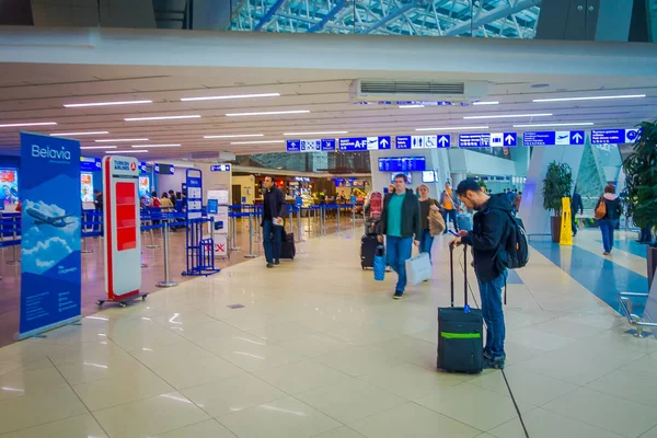 MINSK, BÉLARO - 01 DE MAYO DE 2018: Turistas no identificados caminando con sus maletas y viendo una pantalla de salida, ubicada dentro del aeropuerto de Minsk — Foto de Stock