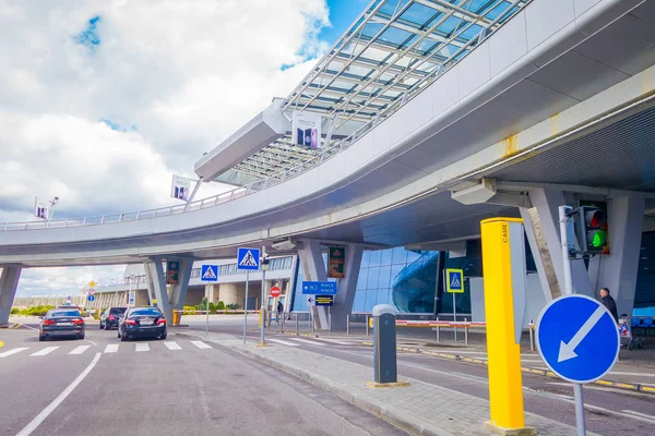 MINSK, BELARUS - 01 DE MAYO DE 2018: Vista de personas caminando y coches estacionados en la entrada del edificio del aeropuerto de Minsk en un día nublado con una estructura de puente apedreado iat la entrada del aeropuerto en Bielorrusia —  Fotos de Stock