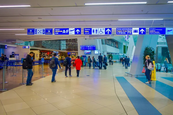 Minsk, Weißrussland - 01. Mai 2018: Unbekannte Touristen gehen mit ihrem Gepäck spazieren und beobachten einen Abflugschirm, der sich im Inneren des Flughafens von Minsk befindet — Stockfoto