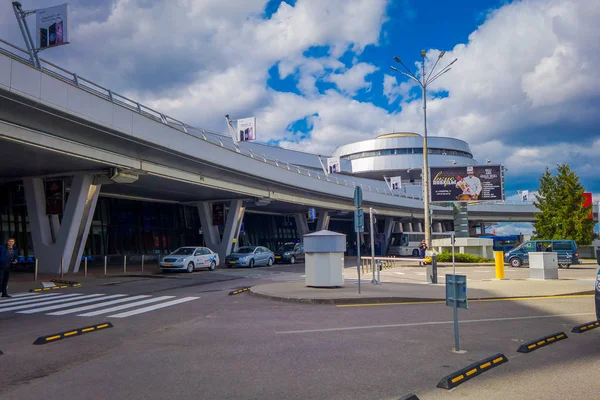 Minsk, Weißrussland - 01. Mai 2018: Außenansicht von geparkten und umlaufenden Autos am Eingang des Flughafengebäudes in Minsk an einem bewölkten Tag mit einem Kontrollturm dahinter — Stockfoto