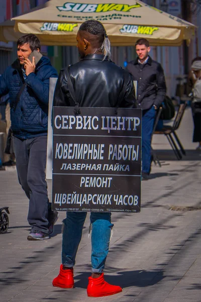 Işıklar Moskova, Rusya - Nisan, 24, 2018: açık bir tabela onun vücudunda giyen ve şenlikli bir Noel altında yürüyüş Tanımlanamayan zenci, görünümünü Nikolskaya sokaklarda — Stok fotoğraf