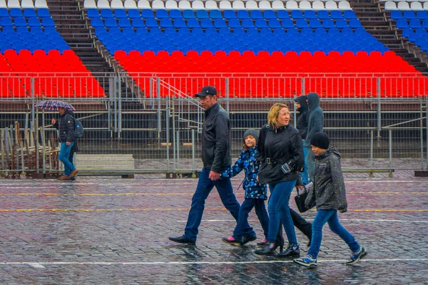 MOSCÚ, RUSIA - 29 DE ABRIL DE 2018: Vista al aire libre de personas no identificadas que usan ropa de abrigo y sostienen paraguas, protegen de la lluvia y caminan en la plaza roja y el hito de la arquitectura en Moscú —  Fotos de Stock