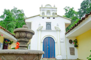 POPAYAN, COLOMBIA - FEBRUARY 06, 2018: Outdoor view of white small cathedral with a stoned fountain in Popayan town, visited for many tourists for be a quite place clipart