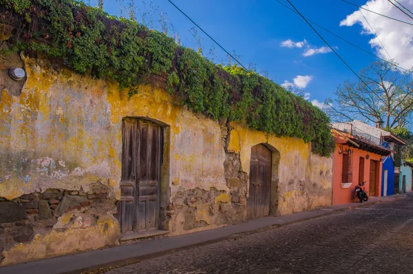 Outdoor view of yellow wall of old building, almost destroyed with some plants over the wall, close to colonial house buildings in Antigua city — Stock Photo, Image