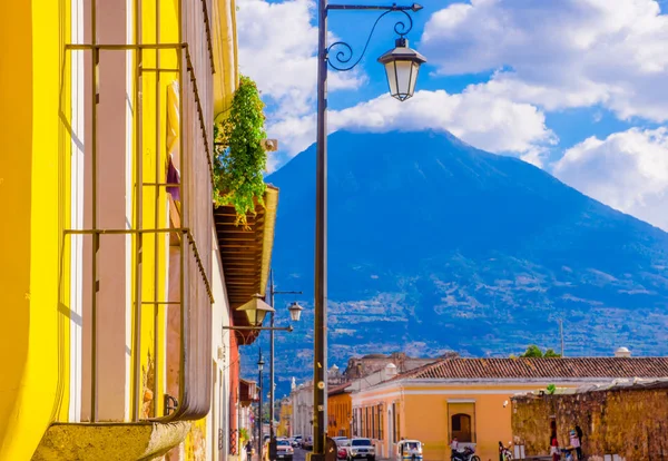 Buiten uitzicht op balkon met sommige planten in een pot en publibc lamp lichten met een vulkaan achter, gedeeltelijke bedekt met wolken in een prachtige zonnige dag in Antigua Guatemala — Stockfoto