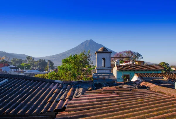 Vacker utomhus utsikt över hustaken i byggnaden i Antigua stad med agua vulkan berget bakom i en vacker solig dag och blå himmel — Stockfoto