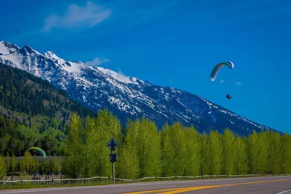 Außenansicht von Menschen, die Gleitschirmfliegen in Grand Tetons im Morgenlicht mit einem riesigen Berg teilweise mit Schnee am Horizont bei herrlichem blauen Himmel bedeckt üben — Stockfoto