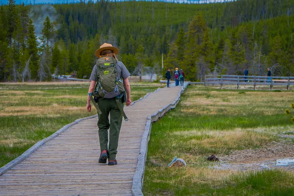 여성 공원 레인저 그린 배낭, 유니폼을 입고 오래 된 충실 한 어퍼 간헐천 분 지에 나무 경로 따라 산책의 옐로스톤, 몬태나, 미국 2018 년 5 월 24 일: 야외 보기 — 스톡 사진