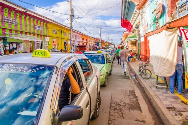 GRANADA, NICARAGUA, MAY, 14, 2018: Cars waiting in the traffic while unidentified people is walking in the street of market stalls at a colorful street in Granada — Stock Photo, Image