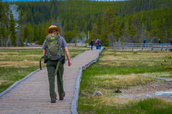 Yellowstone, Μοντάνα, ΗΠΑ 24 Μαΐου 2018: Εξωτερική άποψη της γυναικείας πάρκο δασοφύλακας φορούν μια πράσινη ομοιόμορφο με ένα σακίδιο, το ξύλινο μονοπάτι στην ανώτερη λεκάνη Geyser παλιά πιστοί — Φωτογραφία Αρχείου