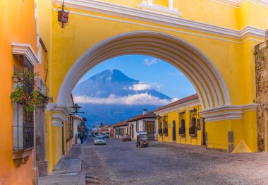 Ciudad de Guatemala, Guatemala, April, 25, 2018: View of the active Agua volcano in the background through a colorful yellow arch of Antigua city in Guatemala clipart