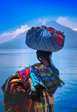 Panajachel, Guatemala-Nisan, 25, 2018: tipik giyim eşyası ve içinde göl kıyısındaki küçük teknelerle Atitlan göl ve arka planda yanardağ ile yürüme unidentifed yerli kadın, açık görünüm