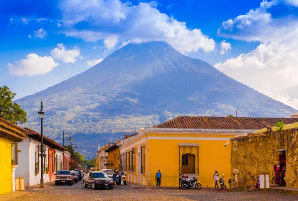 Ciudad de Guatemala, Guatemala, 25 aprile 2018: Veduta della città di Antigua, con alcune auto in attesa su una strada pavimentata tonica, circondata da vecchi edifici e il vulcano Agua sullo sfondo — Foto Stock