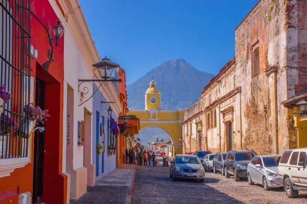 Ciudad de Guatemala, Guatemala, 25 aprile 2018: Turisti non identificati sotto un arco giallo in attesa di autobus nella città di Antigua con il vulcano Agua attivo sullo sfondo — Foto Stock