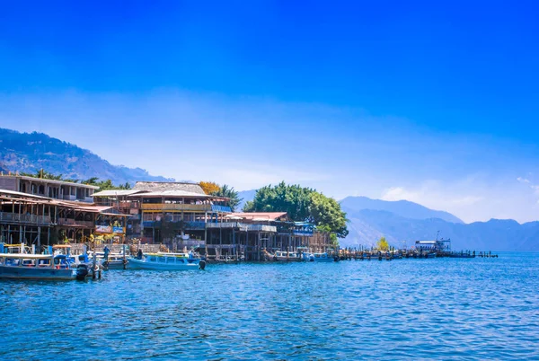 Panajachel, Guatemala-abril, 25, 2018: Vista al aire libre de los barcos en la orilla, pequeño pueblo en el fondo en la orilla, lago Atitlan — Foto de Stock