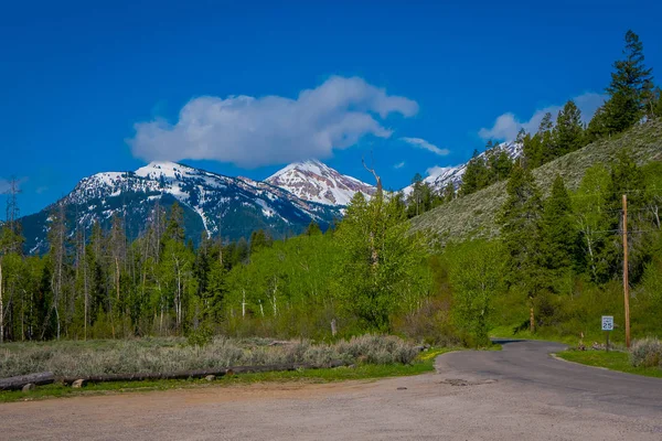 Blick auf den steinigen Highway, der zum Grand Teton Nationalpark führt, in einem herrlichen sonnigen Tag mit schneebedeckten Bergen am Horizont — Stockfoto