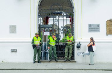 POPAYAN, COLOMBIA - FEBRUARY 06, 2018: Outdoor view of unidentified woman waiting while thre cops are at the enter of a palace or white building in colonial city Popayan clipart