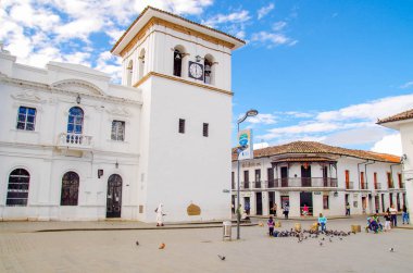 POPAYAN, COLOMBIA - FEBRUARY 06, 2018: Unidentified people walking in the quare in front of the clock tower in Popayan, during a sunny day, gorgeous blue sky background clipart