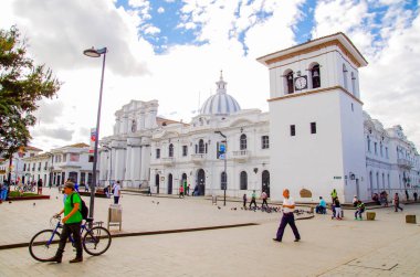 POPAYAN, COLOMBIA - FEBRUARY 06, 2018: Unidentified people walking in the quare in front of the clock tower in Popayan, during a sunny day, gorgeous blue sky background clipart