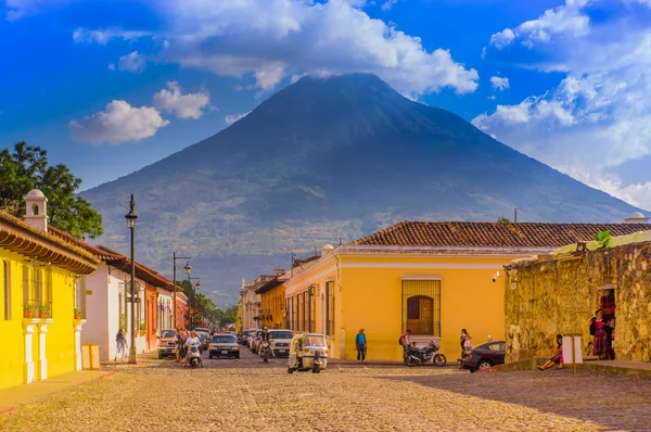 Ciudad de Guatemala, Guatemala, 25 aprile 2018: Veduta della città di Antigua, con alcune auto in attesa su una strada pavimentata tonica, circondata da vecchi edifici e il vulcano Agua sullo sfondo — Foto Stock