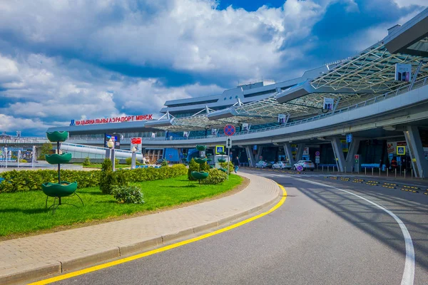 MINSK, BELARUS - 01 DE MAYO DE 2018: Vista al aire libre de los coches estacionados en la entrada del edificio del aeropuerto de Minsk en un día nublado con algunas plantas en un pequeño jardín en frente — Foto de Stock