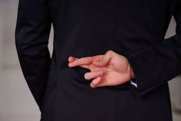 Close up of man wearing a suit, and crossing his fingers, in a blurred background — Stock Photo, Image