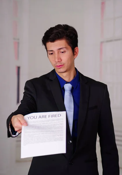 Gros plan d'un jeune homme d'affaires triste portant un costume et tenant une feuille de papier provenant du patron, avec un texte tiré dessus, dans un arrière-plan flou — Photo