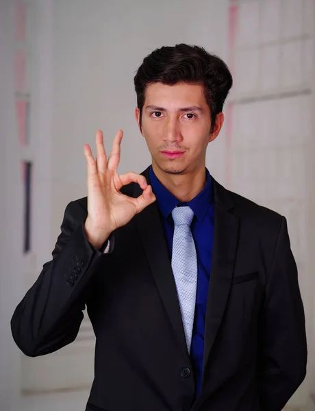 Close up of businessman wearing a suit, doing a sign of ok with his hand, in a blurred background — Stock Photo, Image