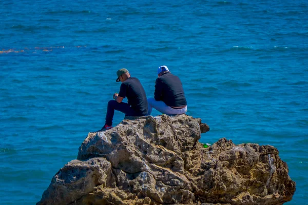 Los Ángeles, California, Estados Unidos, 15 de junio de 2018: Vista al aire libre de amigos no identificados hablando y sentados sobre una roca en la playa de Malibú California — Foto de Stock