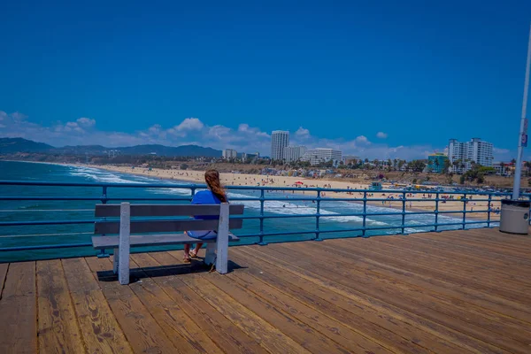Los Angeles, Kalifornie, Usa, 15 června 2018: Žena sedí v křesle dřevěná lavice na mostě dohlíží pláže v Santa Monice v Kalifornii Usa během slunečného dne — Stock fotografie