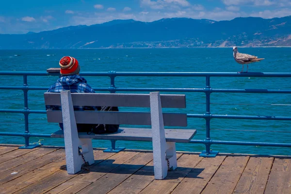 Los Ángeles, California, Estados Unidos, 15 de junio de 2018: Hombre no identificado sentado en una silla de banco de madera en el puente que supervisa Santa Monica Beach en California, Estados Unidos durante el día soleado — Foto de Stock