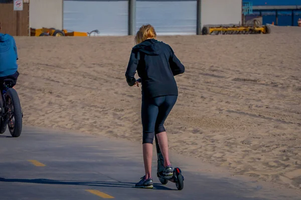 Los Ángeles, California, Estados Unidos, 15 de junio de 2018: Vista al aire libre de una mujer no identificada usando una scooter en Venice Beach en Santa Mónica, popular por los residentes domésticos para relajarse y practicar deporte — Foto de Stock