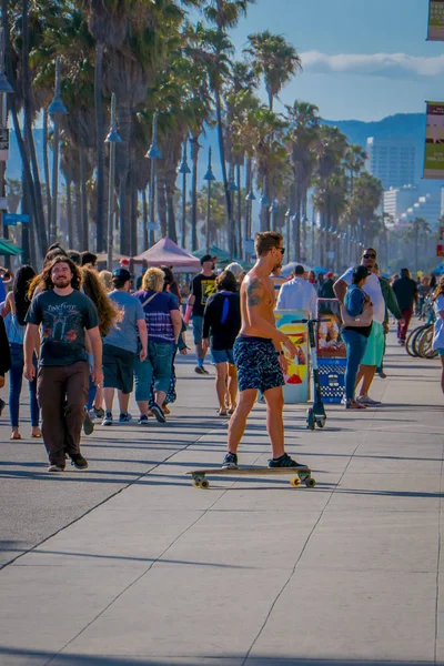 Los Angeles, California, USA, JUNE, 15, 2018: Outdoor view of unidentified people walk along the Venice Beach and young skateboarder with his skate in a path walk — Stock Photo, Image