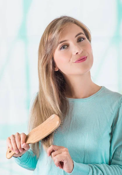 Primer plano de una hermosa mujer joven cepillándose el pelo en un fondo borroso — Foto de Stock