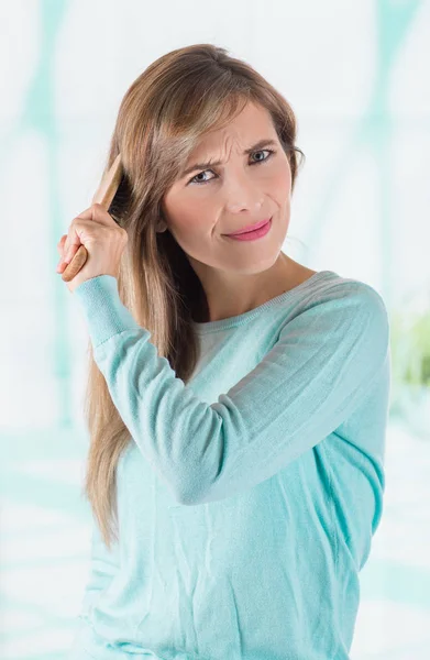 Close up of a mad woman wearing a soft blue blouse and brushing her hair in a blurred background — Stock Photo, Image